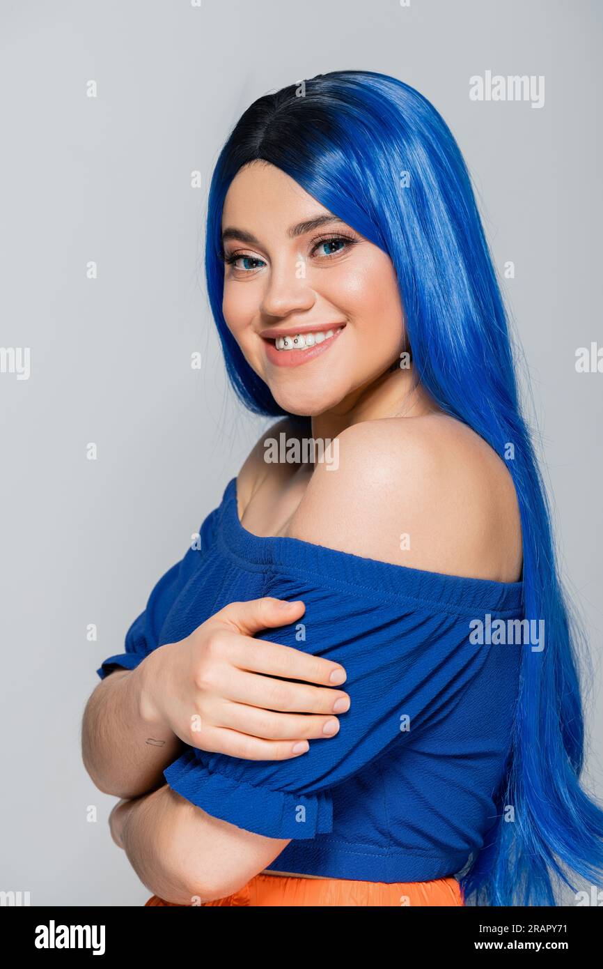 positivité et tendances de beauté, jeune femme tatouée avec des cheveux teints souriant sur fond gris, coiffure, cheveux bleus, beauté moderne, expression de soi, po Banque D'Images