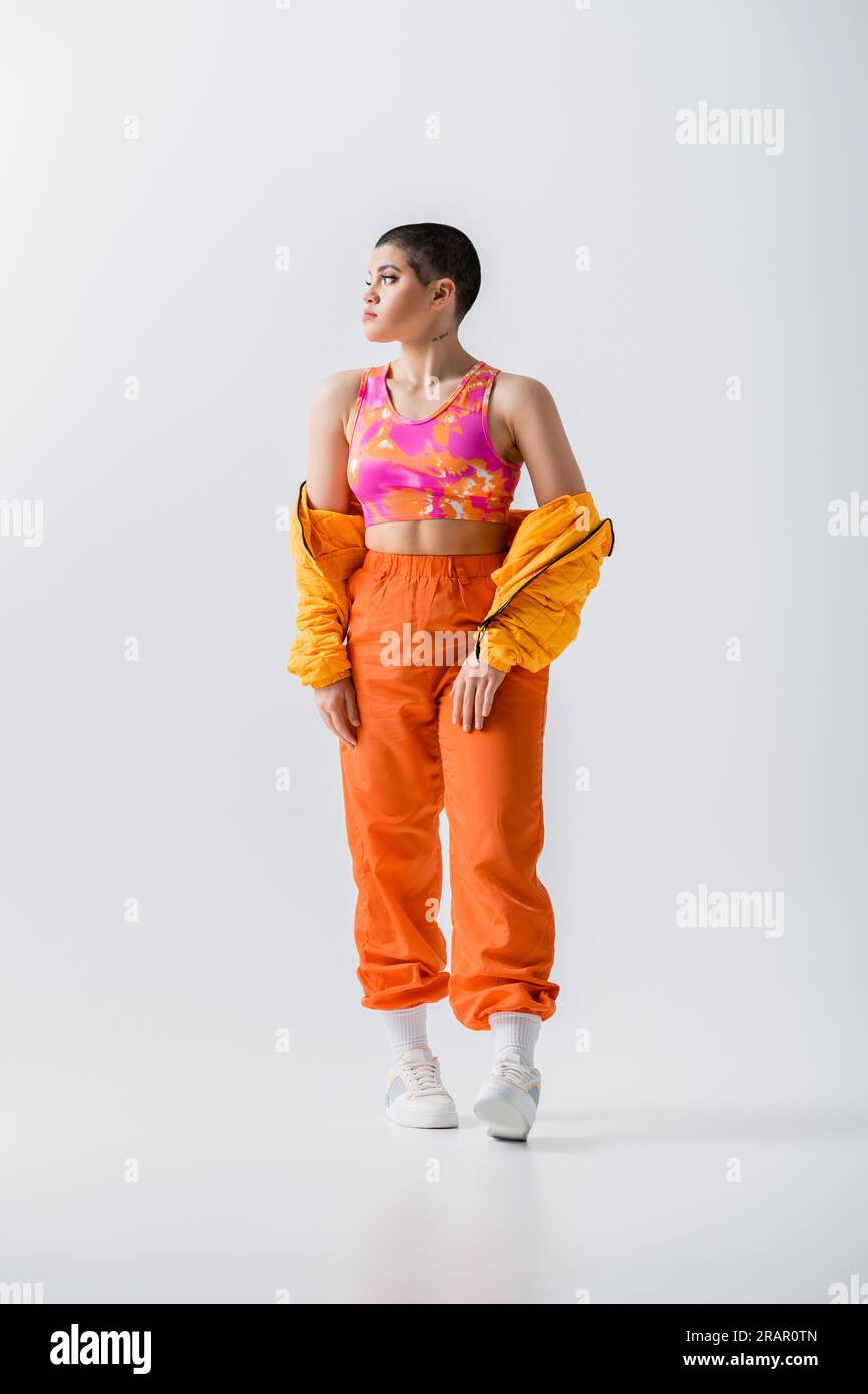 generation z jeune femme a la mode avec une paire courte posant dans une veste bouffante et un pantalon vibrant sur fond gris regardant loin vetements d exterieur su moderne Photo Stock