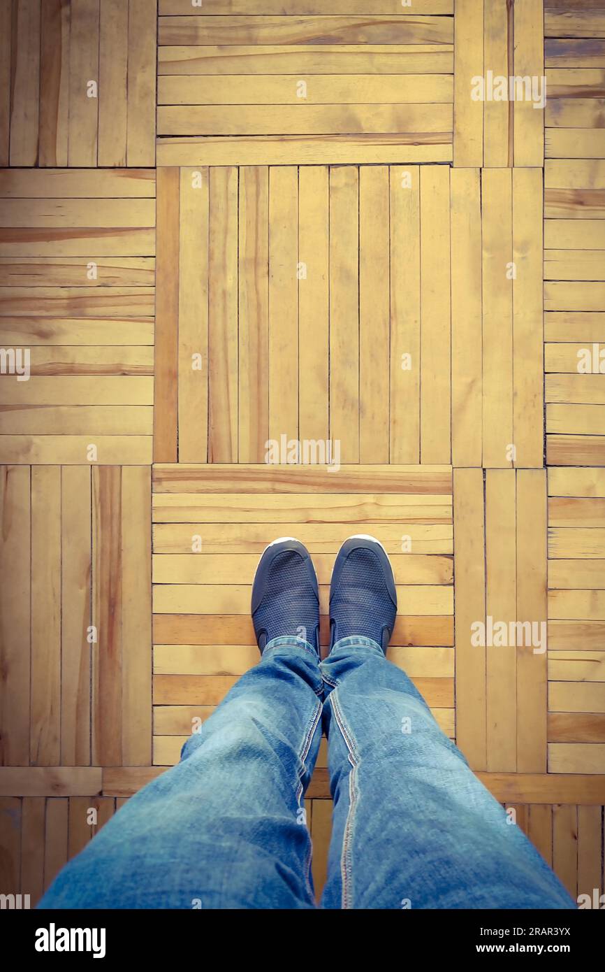 Cliché recadré de jambes masculines debout dans des baskets sur parquet en bois Banque D'Images