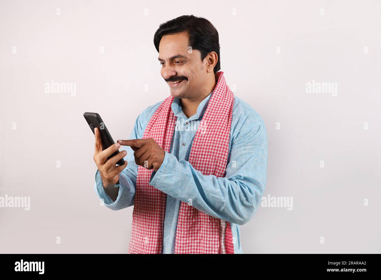 Portrait de l'homme fermier indien heureux dans le concept de l'Inde rurale. fond blanc. Fermier joyeux regardant dans l'écran du téléphone portable, en utilisant la technologie Banque D'Images