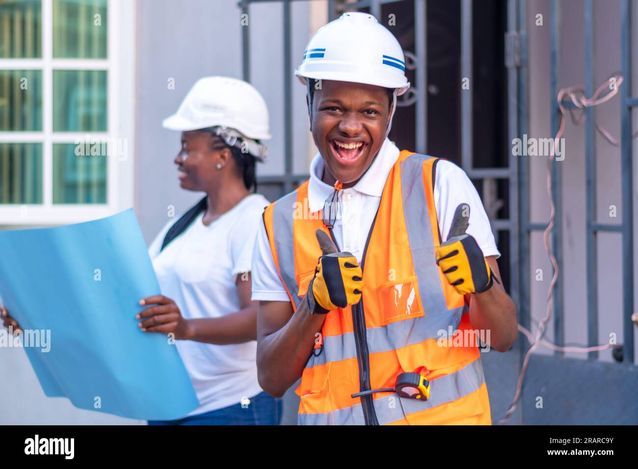 Heureux ingénieur africain portant un casque de sécurité et une veste réfléchissante avec les deux pouces vers le haut, donnant signe positif d'approbation, pouce vers le haut geste Banque D'Images