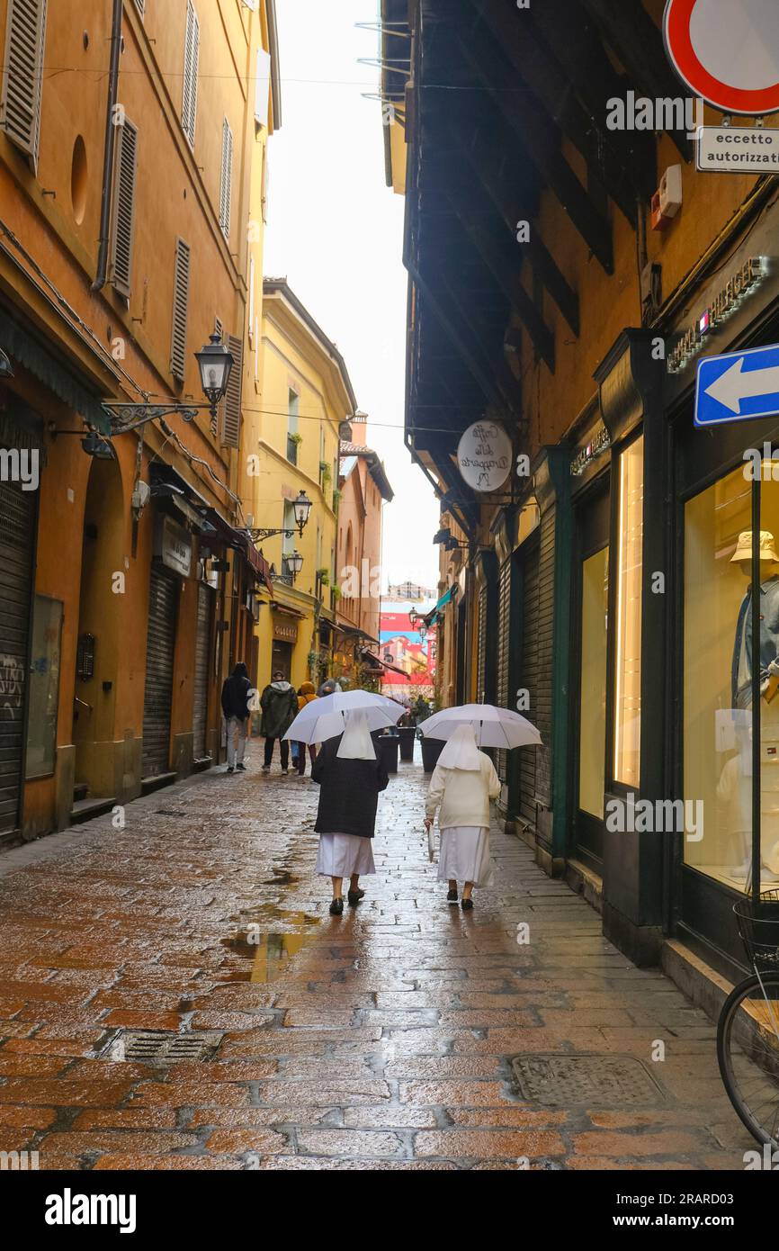 Deux nonnes avec des parapluies blancs marchant dans la rue étroite de Bologne, Italie sous la pluie Banque D'Images