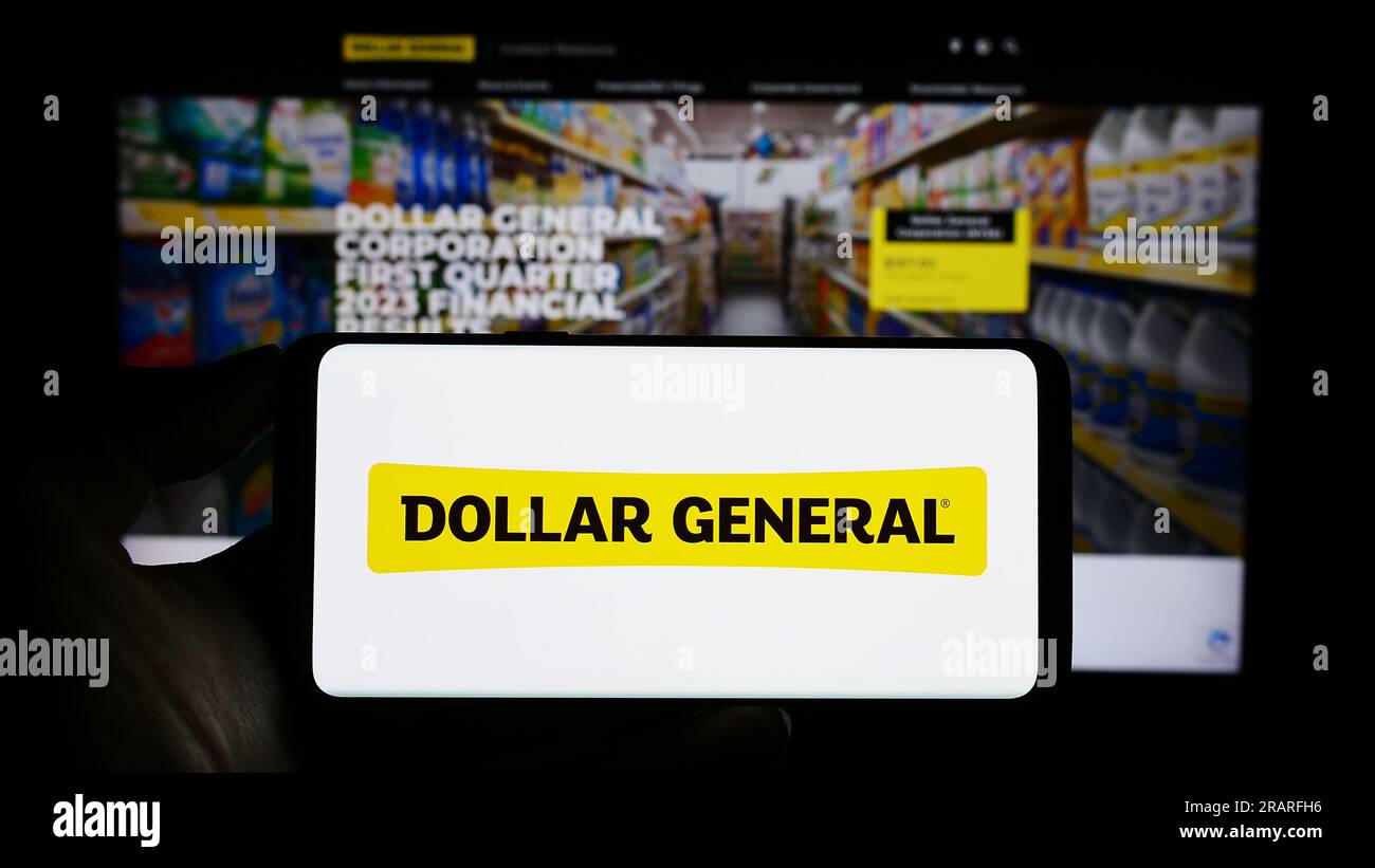 Personne tenant le smartphone avec le logo de la société de détail américaine Dollar General Corporation sur l'écran devant le site Web. Concentrez-vous sur l'affichage du téléphone. Banque D'Images