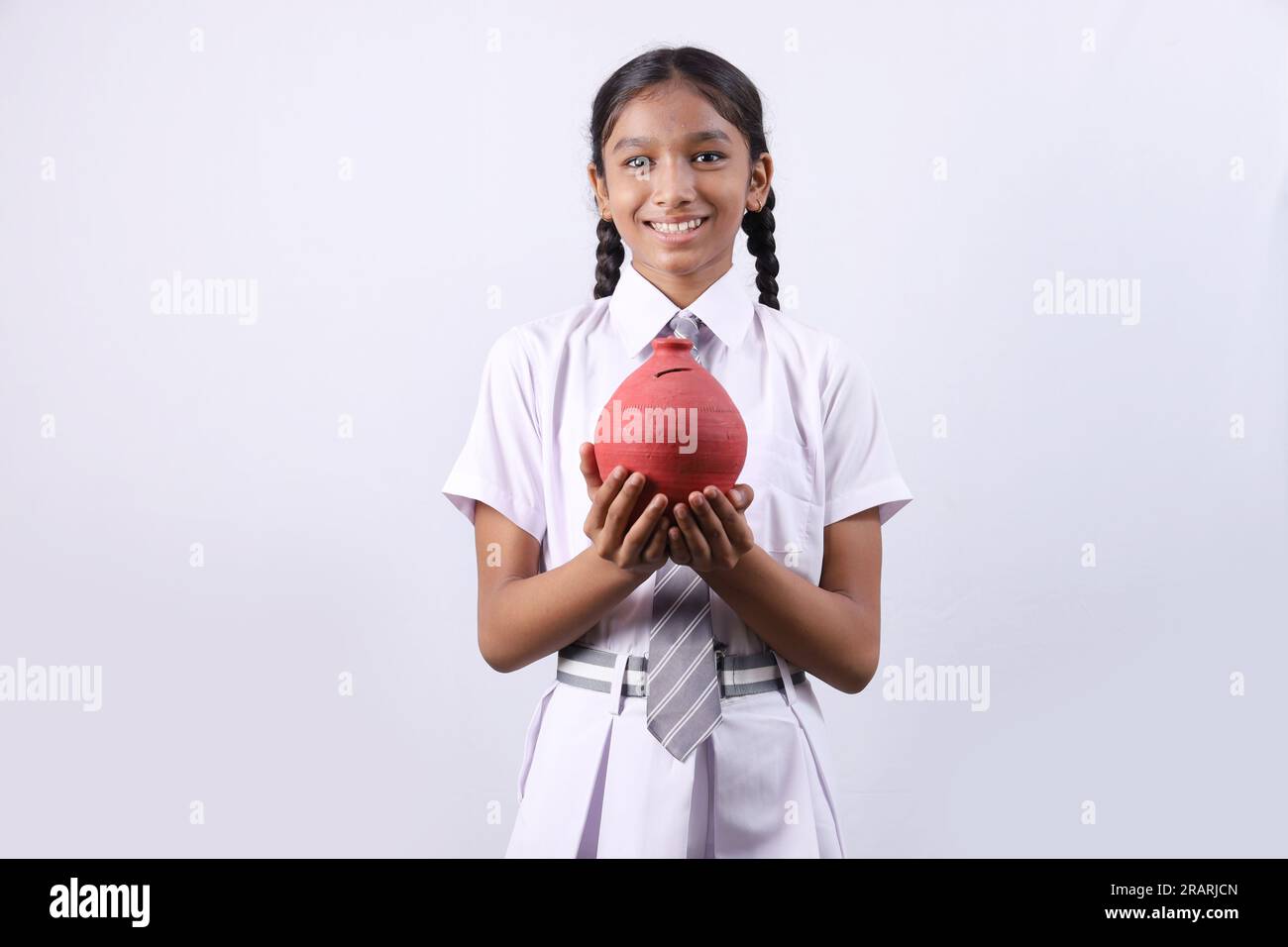 Heureuse fille d'école indienne tenant une tirelire en main présentant joyeusement diverses humeurs d'économiser de l'argent et des concepts bancaires Banque D'Images