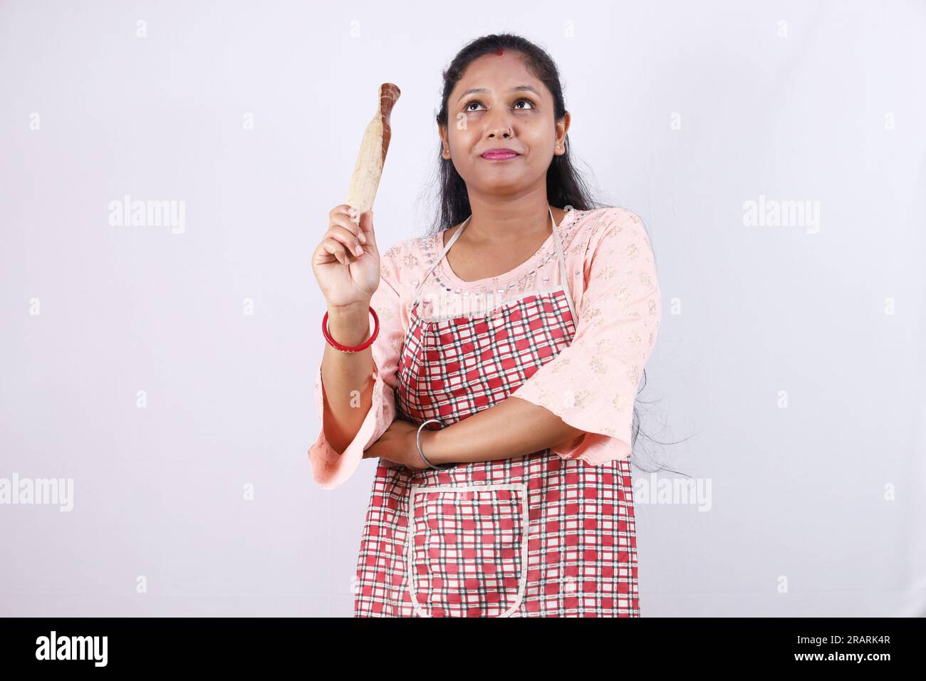 Heureuse femme au foyer indienne tenant un rouleau à pâtisserie dans la main et portant une casquette de chef mettant en valeur diverses humeurs du chef de la maison portant un tablier. Banque D'Images