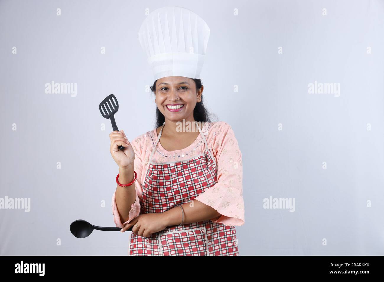 Heureuse femme au foyer indienne tenant une cuillère à frire à la main et portant un chapeau de chef mettant en valeur diverses humeurs du chef de la maison portant un tablier. Banque D'Images