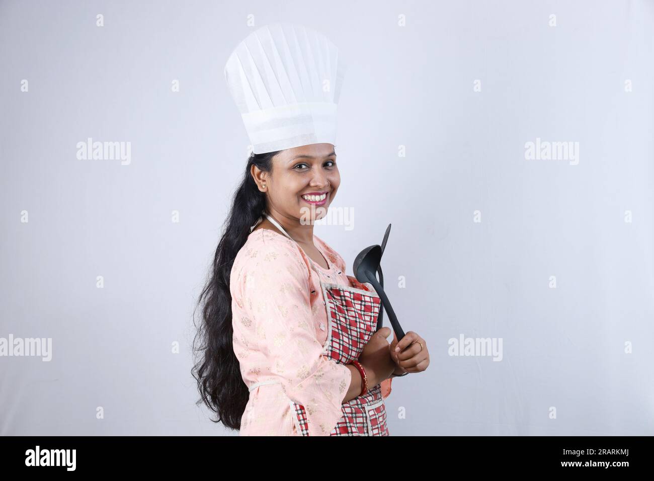 Heureuse femme au foyer indienne tenant une cuillère à frire à la main et portant un chapeau de chef mettant en valeur diverses humeurs du chef de la maison portant un tablier. Banque D'Images