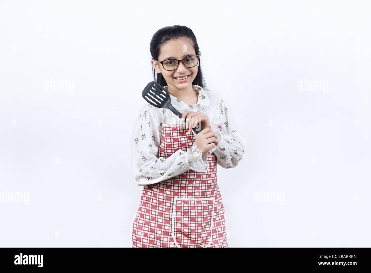 Portrait d'une adolescente indienne heureuse dans la cuisine tenant des accessoires de cuisine. Rolling Rin, cuillère à frire, louche, poêle à frire. Joyeux et joyeux jeune Banque D'Images