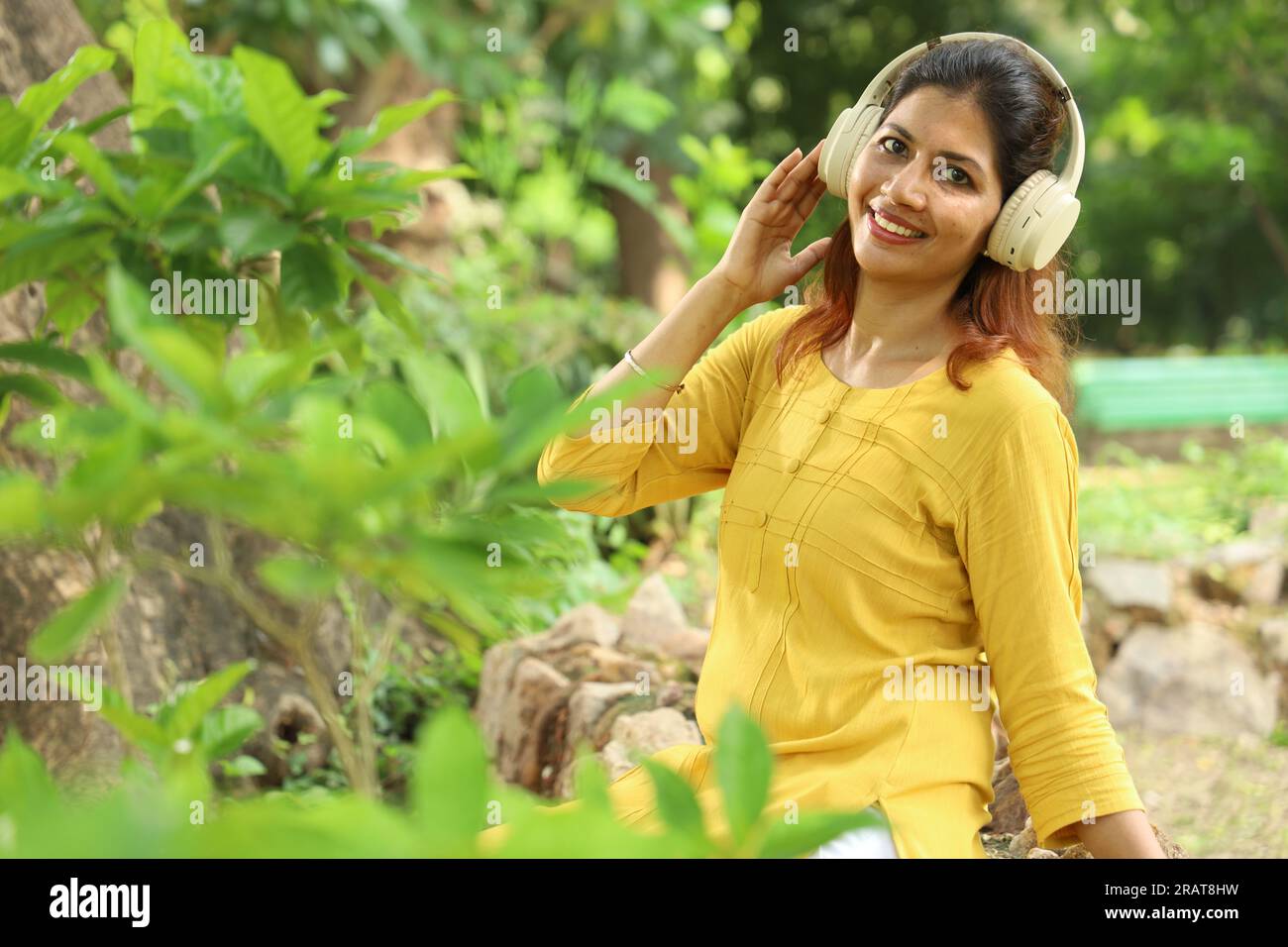 Slim Belle femme écoutant et appréciant de la musique dans un parc à l'aide d'écouteurs sous l'arbre parmi les verts. Concept musical. Banque D'Images