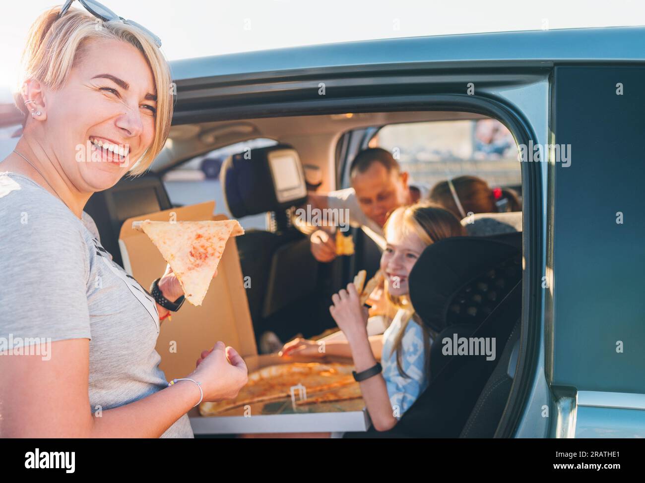 Femme souriante positive avec une tranche de pizza italienne juste cuite pendant que voyage en voiture familiale s'arrête. Heureux moments en famille, enfance, restauration rapide, famille v Banque D'Images