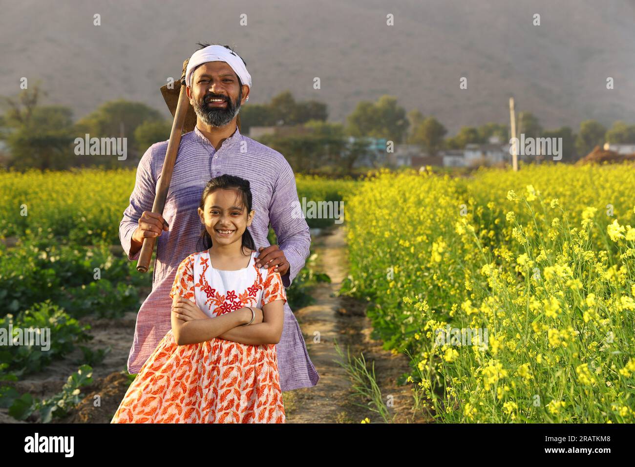 Beau portrait dramatique d'un fermier indien en colère rural et sa fille debout dans le champ de moutarde portant kurta pyjama tenant la pelle à la main. Banque D'Images