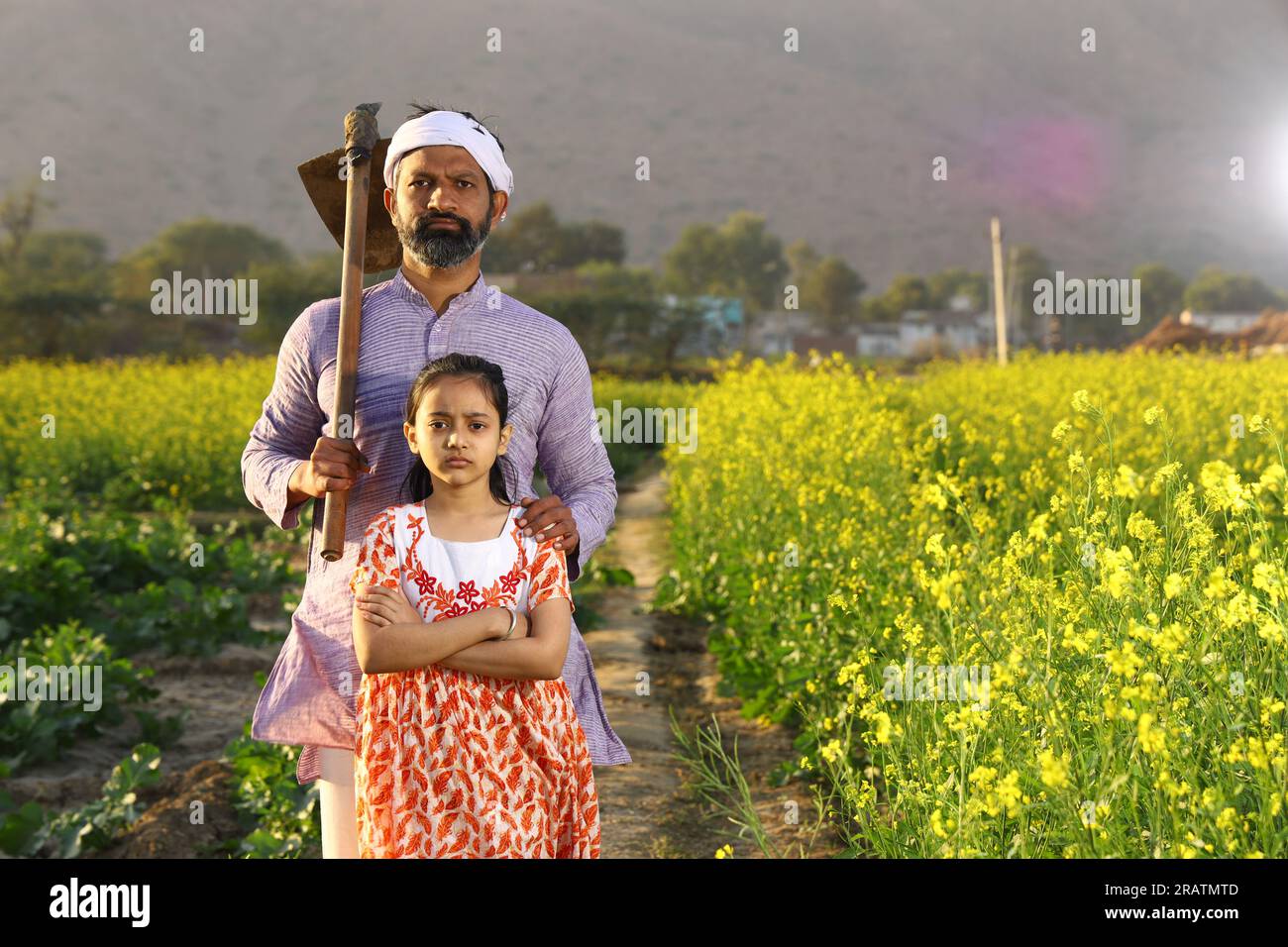 Beau portrait dramatique d'un fermier indien en colère rural et sa fille debout dans le champ de moutarde portant kurta pyjama tenant la pelle à la main. Banque D'Images