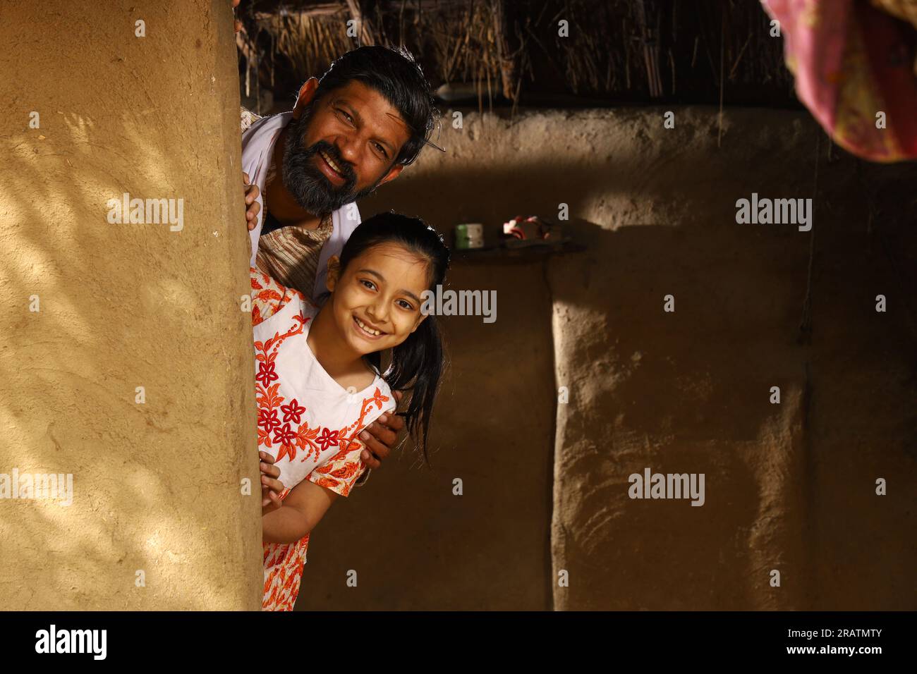 Heureux père indien et fille jouant à cache-cache. Père célibataire avec sa fille qui regarde joyeusement hors de leur chalet dans l'Inde rurale. Banque D'Images