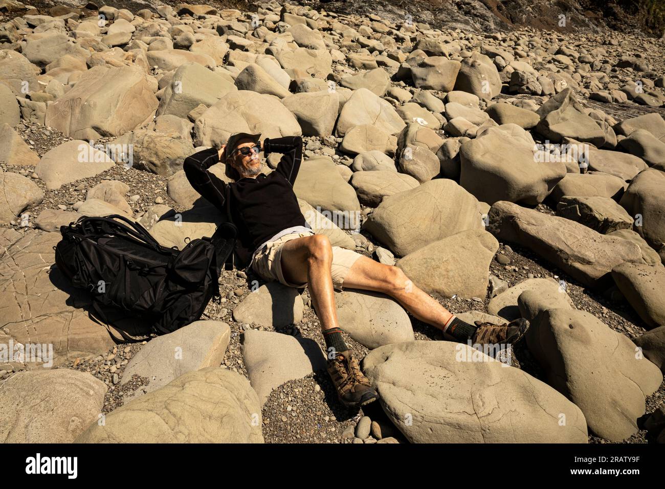 WA23464-00...WASHINGTON - Tom profite du soleil tout en se relaxant sur une plage couverte de rochers au nord de Hole-in-the-Wall dans le parc national olympique. Banque D'Images