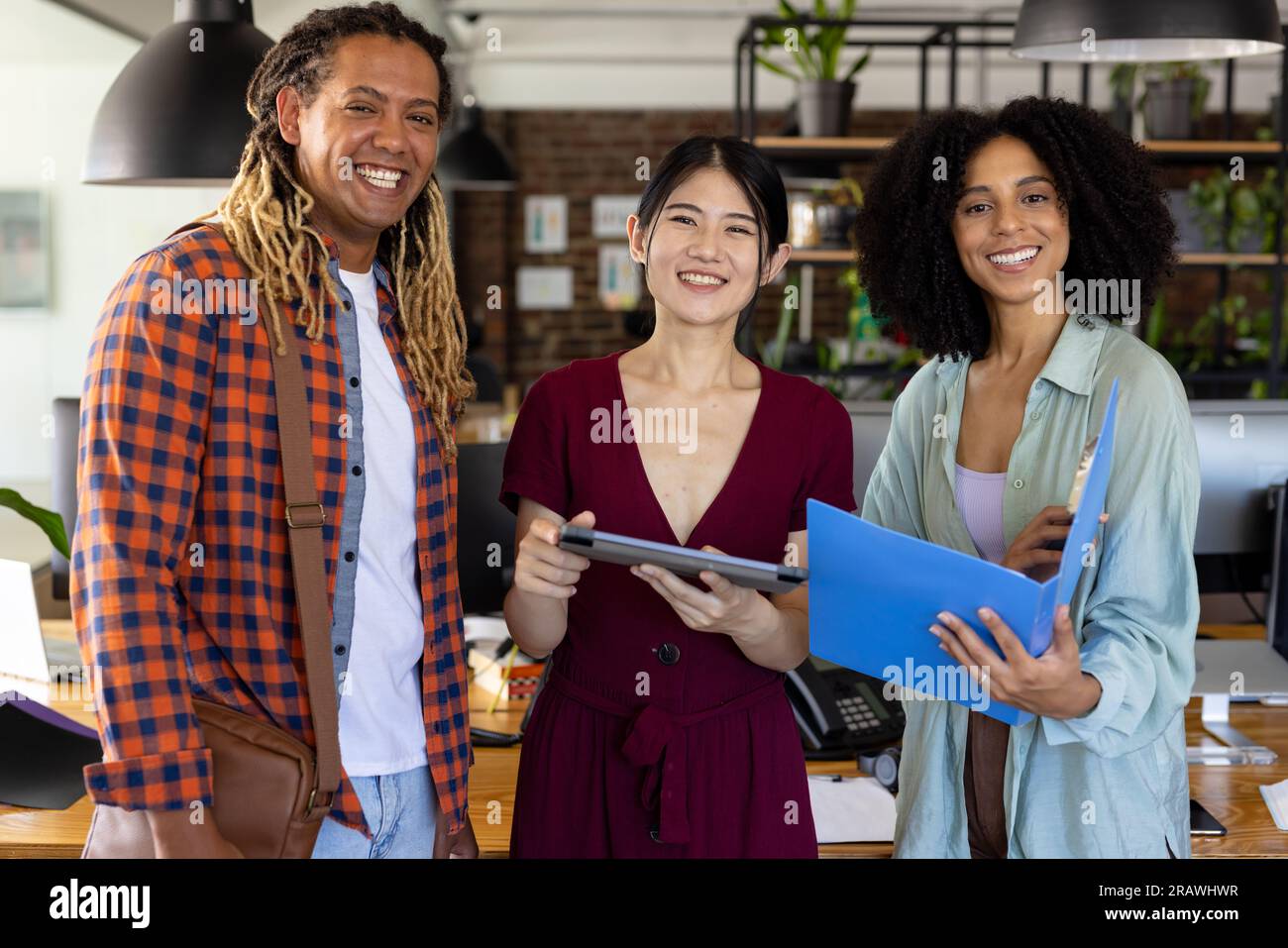 Portrait d'heureux collègues d'affaires occasionnels divers debout dans le bureau ensoleillé avec tablette et dossier. Travail d'équipe, travail, affaires et bureau occasionnel, unal Banque D'Images