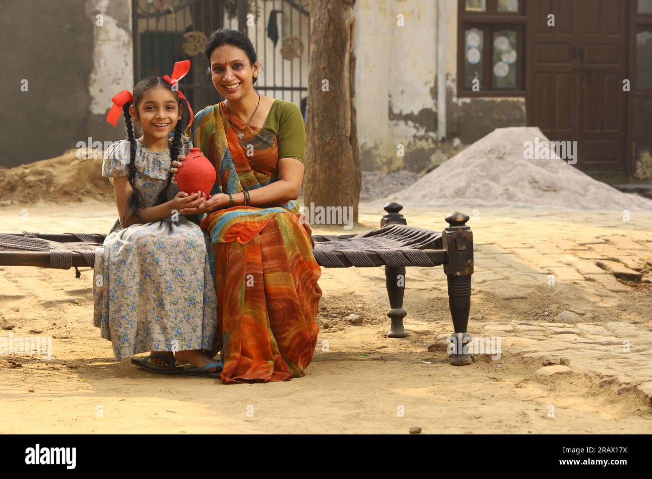 Femme assise avec sa fille dans l'environnement rural portant un Saree qui est la robe traditionnelle pour les femmes dans le nord de l'Inde dans la journée tenant un ordinateur portable Banque D'Images