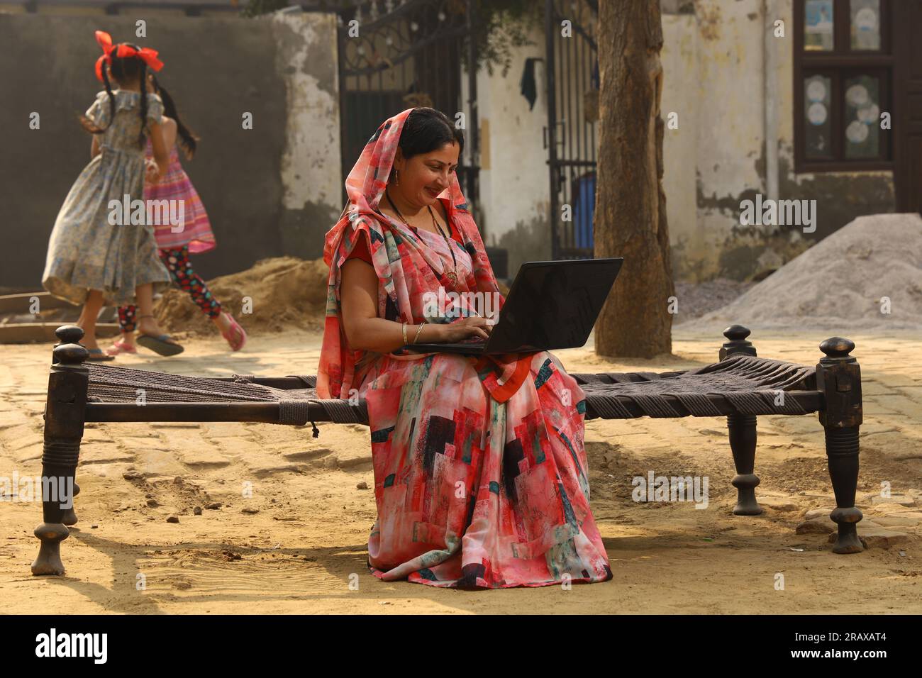 Heureuse femme rurale indienne dans le village. elle est assise sur le lit souriant dehors dans belle saree. Culture indienne, robe traditionnelle, surf sur un ordinateur portable Banque D'Images