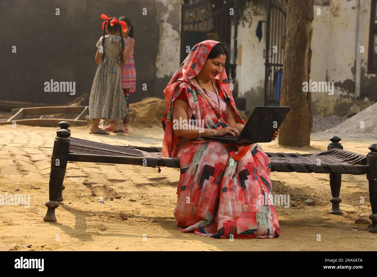 Heureuse femme rurale indienne dans le village. elle est assise sur le lit souriant dehors dans belle saree. Culture indienne, robe traditionnelle, surf sur un ordinateur portable Banque D'Images