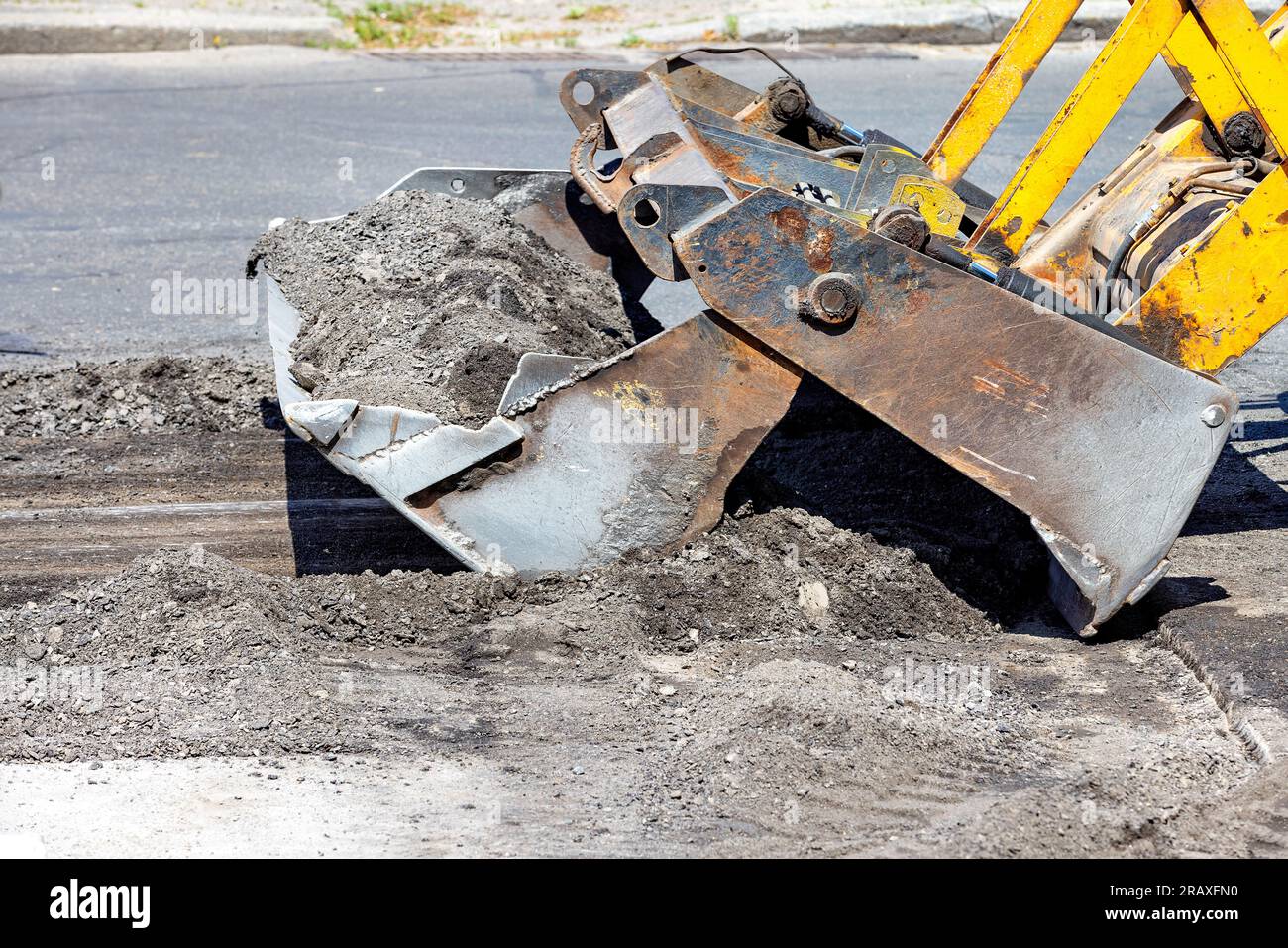 Un puissant godet en métal d'un bulldozer de route ratisse le vieux yasfalt de la surface de la section réparée de la route en un tas. Espace de copie. Banque D'Images