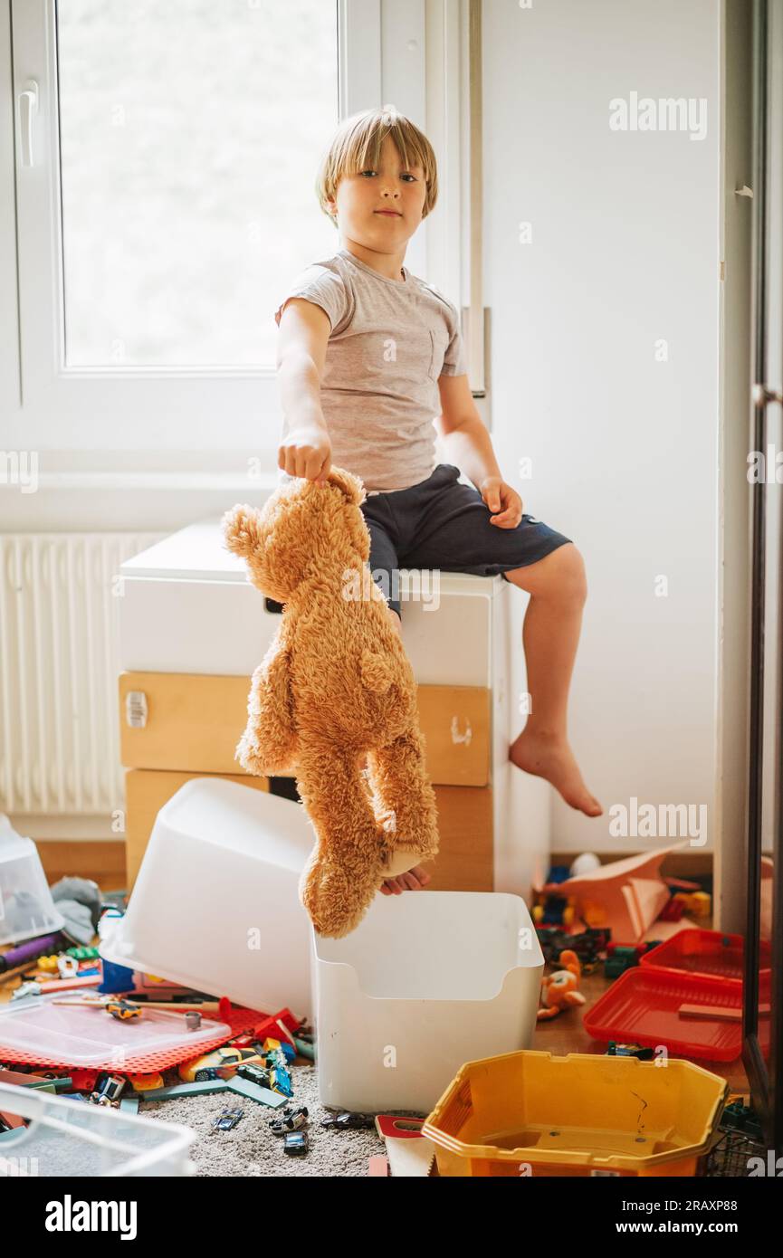 Portrait intérieur d'un enfant jouant dans une pièce très désordonnée, jetant un ours en peluche sur le sol Banque D'Images