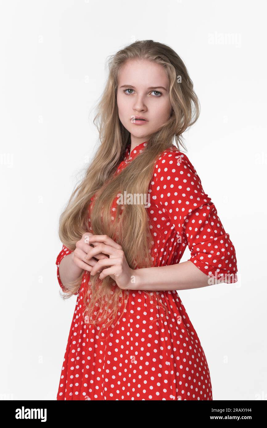 Élégante jeune femme blonde avec les cheveux longs habillée en robe à pois rouge d'été pose sur fond blanc. Ethnie caucasienne femme de 21 ans Banque D'Images