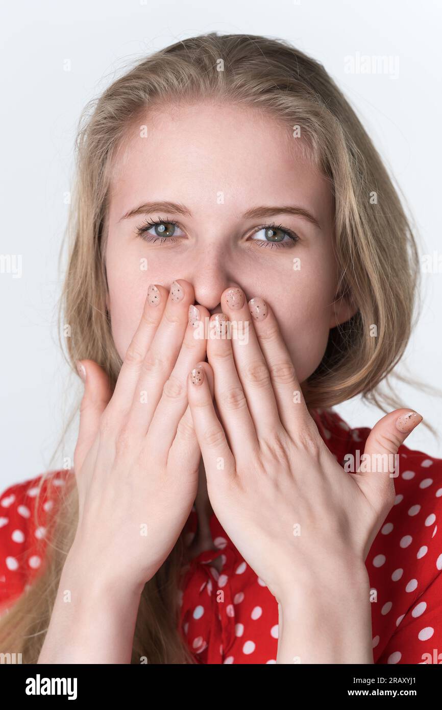 Femme blonde couvre sa bouche avec ses mains et regardant la caméra. Portrait de 21 ans authentique modèle féminin habillé en robe rouge d'été Banque D'Images