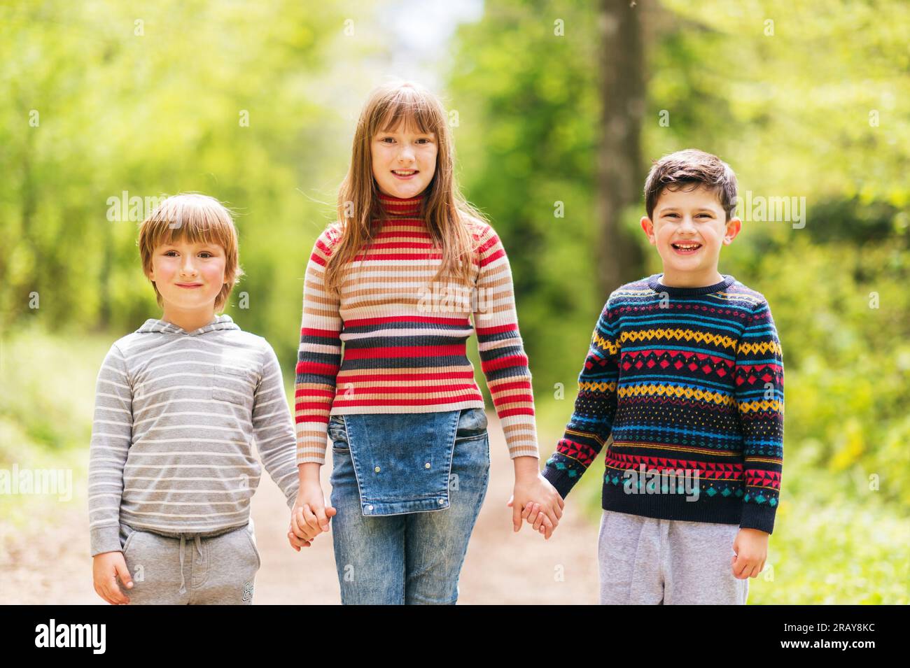 Groupe de trois enfants heureux en randonnée dans la forêt printanière, deux garçons et une fille jouant ensemble à l'extérieur, portant des pull-overs Banque D'Images
