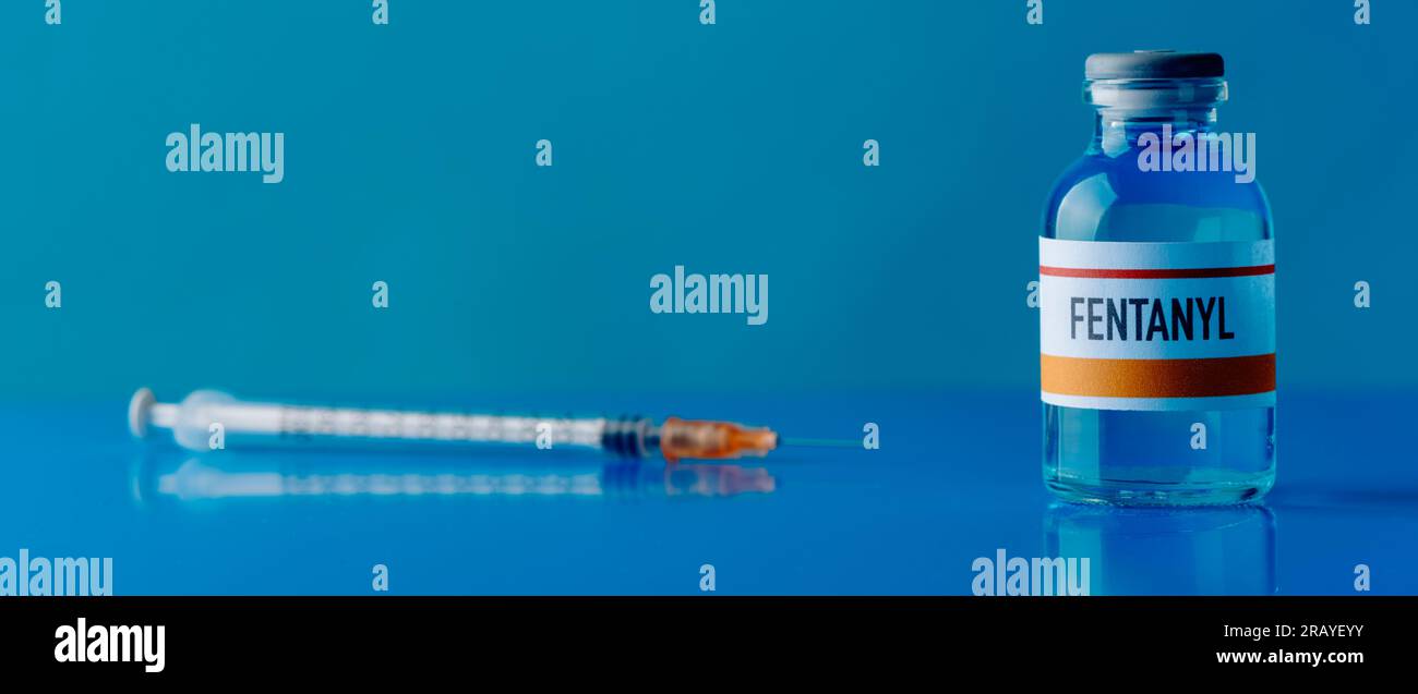 une seringue et un flacon simulé de fentanyl sur une table bleue, dans un format panoramique à utiliser comme bannière web ou en-tête Banque D'Images