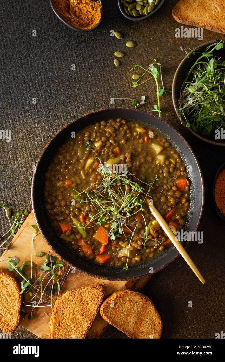 Déjeuners végétariens sains, soupe de lentilles brune avec tomates et carottes, pommes de terre et épices de curry, croûtons grillés, bol avec soupe sur planche à découper Banque D'Images