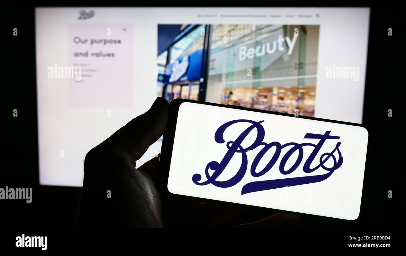 Personne tenant le smartphone avec le logo de la société pharmaceutique britannique Boots UK Limited sur l'écran en face du site Web. Concentrez-vous sur l'affichage du téléphone. Banque D'Images