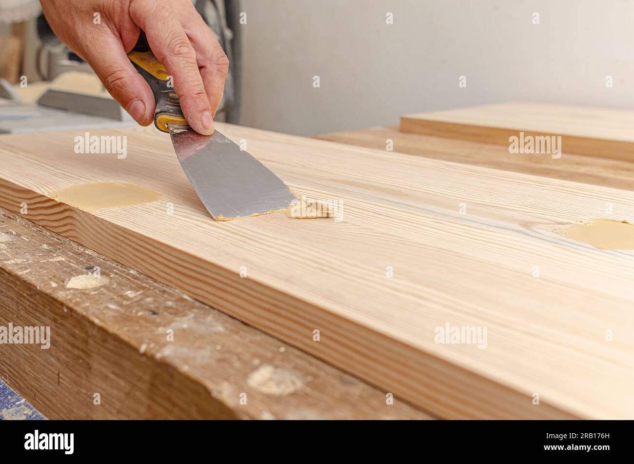 Couvrir les nœuds sur une planche de bois avec du mastic. Spatule, mastic, planche de bois. Les mains de Carpenter. Banque D'Images