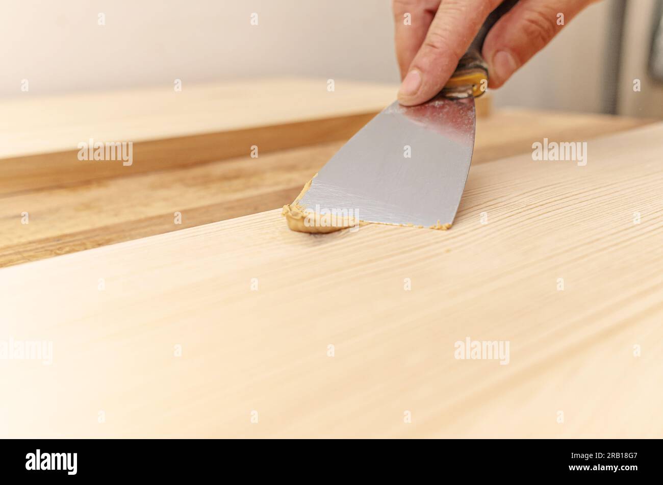 Couvrir les nœuds sur une planche de bois avec du mastic. Spatule, mastic, planche de bois. Les mains de Carpenter. Banque D'Images