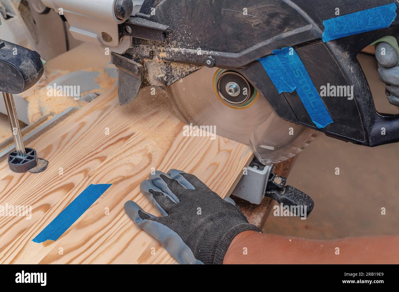 Procédé de découpe de planches de bois avec scie circulaire. La main de charpentier dans le gant. Banque D'Images