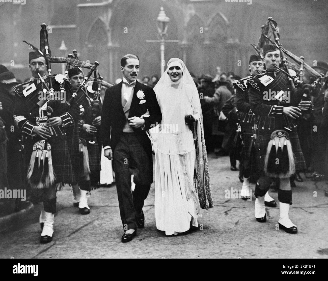 Angleterre : c. 1930 Une mariée et un marié étant accompagnés d'un ensemble cornemuse. Banque D'Images