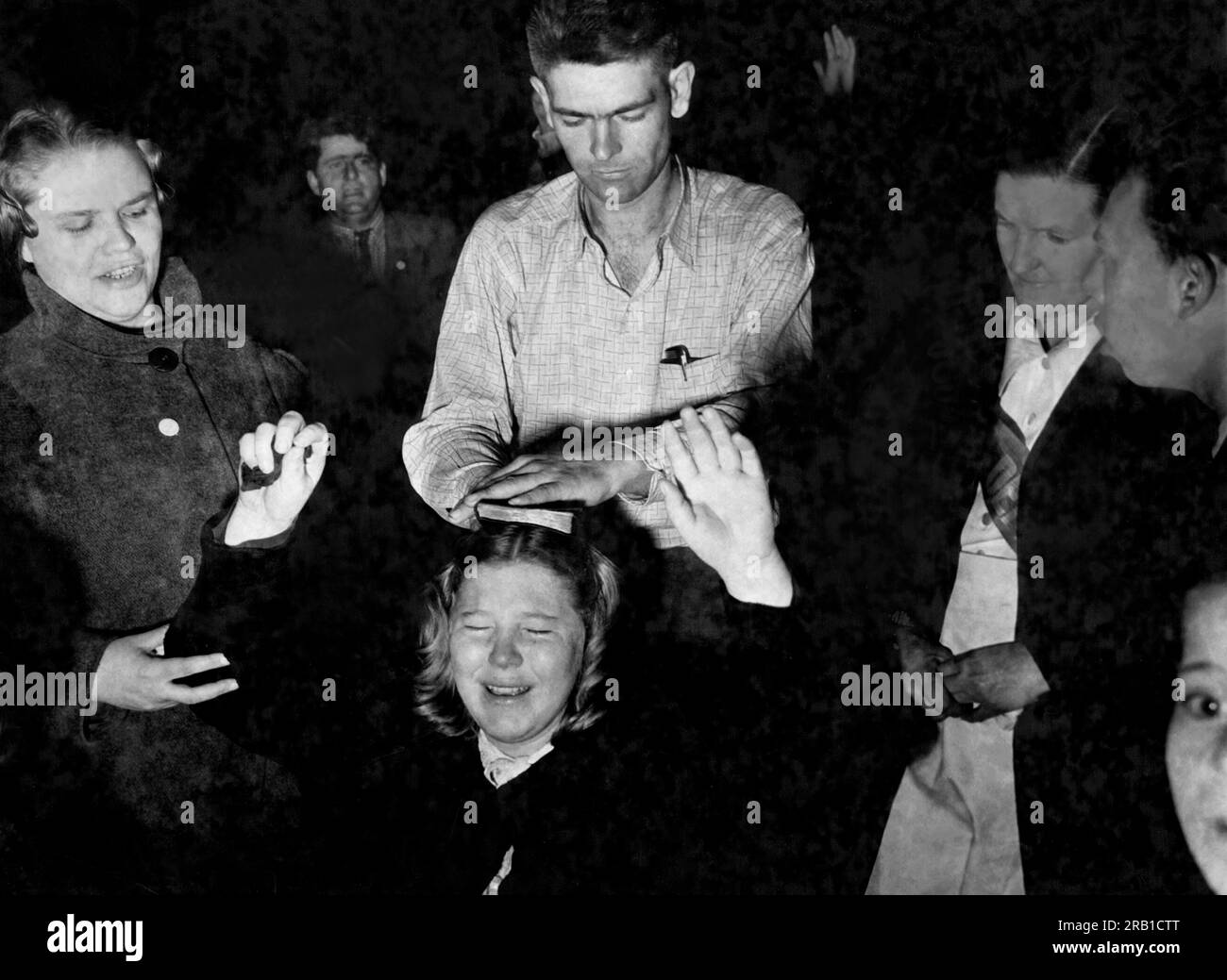 États-Unis : c. 1948 Un homme place une bible sur la tête d'un adorateur extatique agenouillé répondant à l'appel du prédicateur lors d'une réunion de réveil de tente religieuse. Banque D'Images