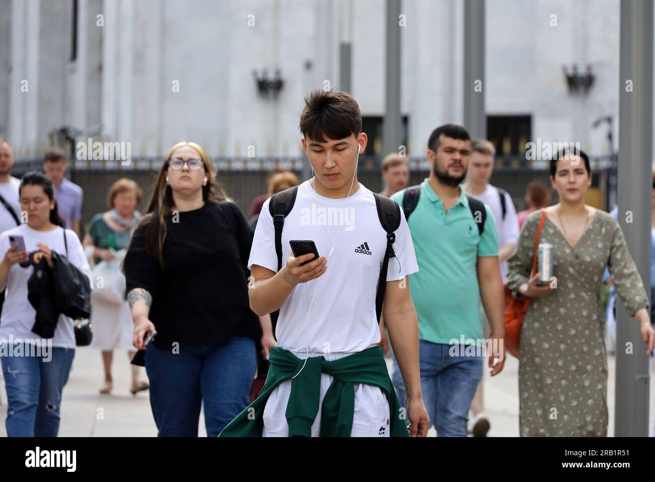 Gars asiatique avec téléphone portable marchant dans la rue de la ville sur fond de gens en été Banque D'Images
