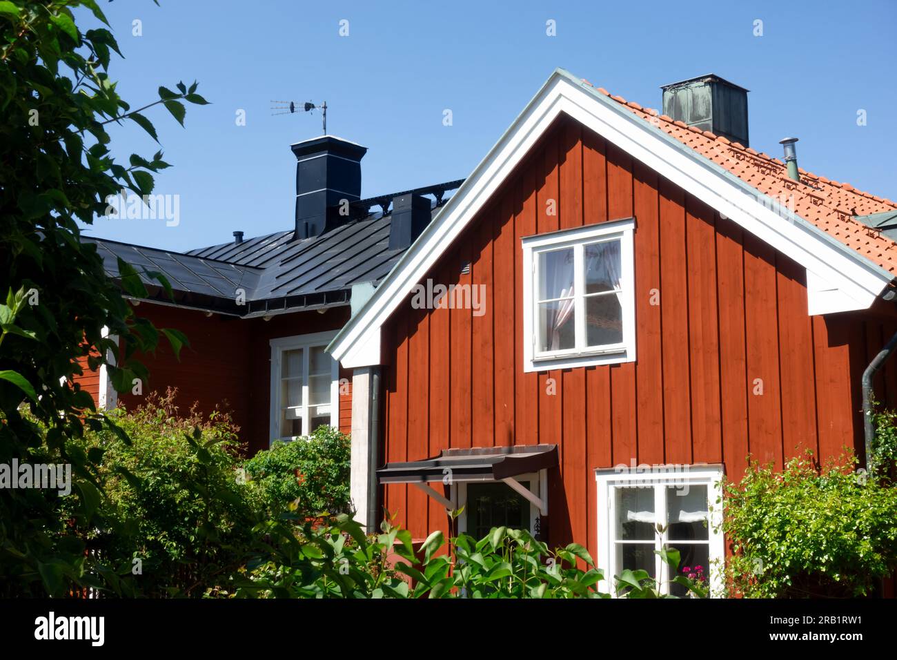 Pignon d'une maison traditionnelle rouge falu vintage avec des coins blancs et des garnitures dans l'archipel suédois rural de Stockholm avec jardin vert luxuriant en été Banque D'Images