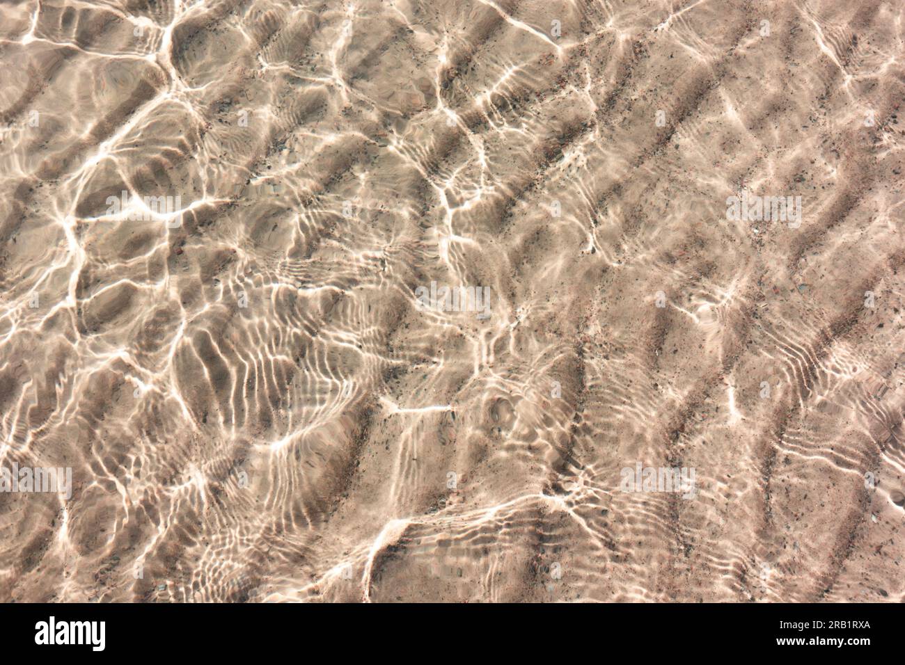 Motif de sable blanc sous l'eau transparente claire avec réflexion du soleil dans les petites vagues de la plage paradisiaque Banque D'Images