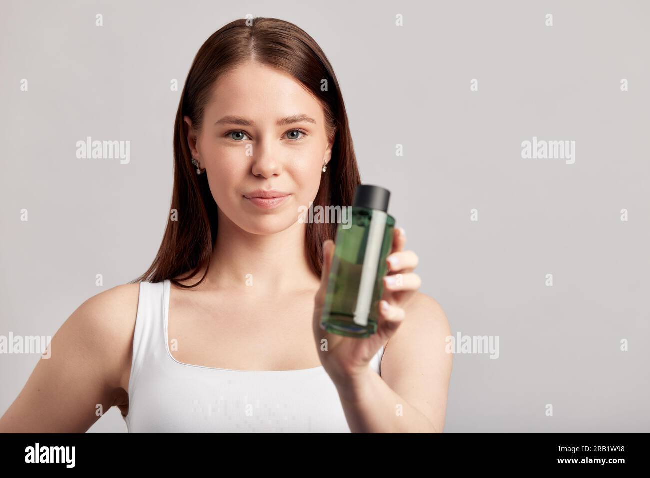 Jeune fille attrayante avec de longs cheveux bruns tient une bouteille de lavage du visage. Femme caucasienne prenant soin de la peau pour maintenir son appétit jeune et sain Banque D'Images