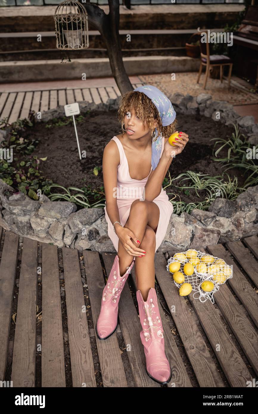 Tendance jeune femme afro americaine en tenue d ete croisant les jambes et tenant le citron frais tout en etant assis pres du sac de maille dans le jardin interieur femme chic dans Photo