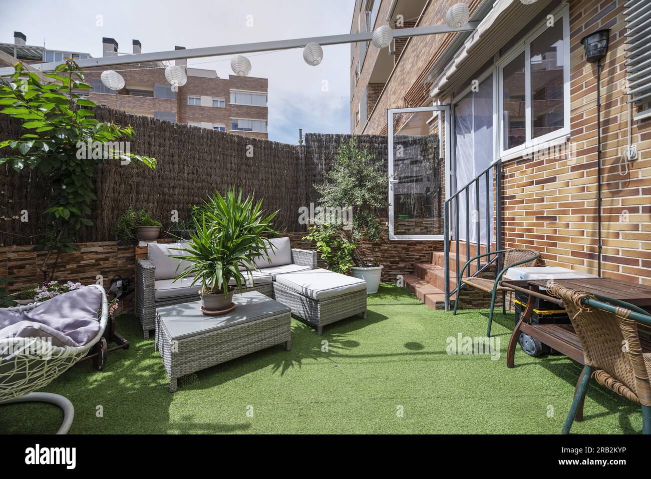 terrasse avec un canapé en raphia, sols en gazon synthétique, aller avec treillis de canne et de nombreuses plantes Banque D'Images