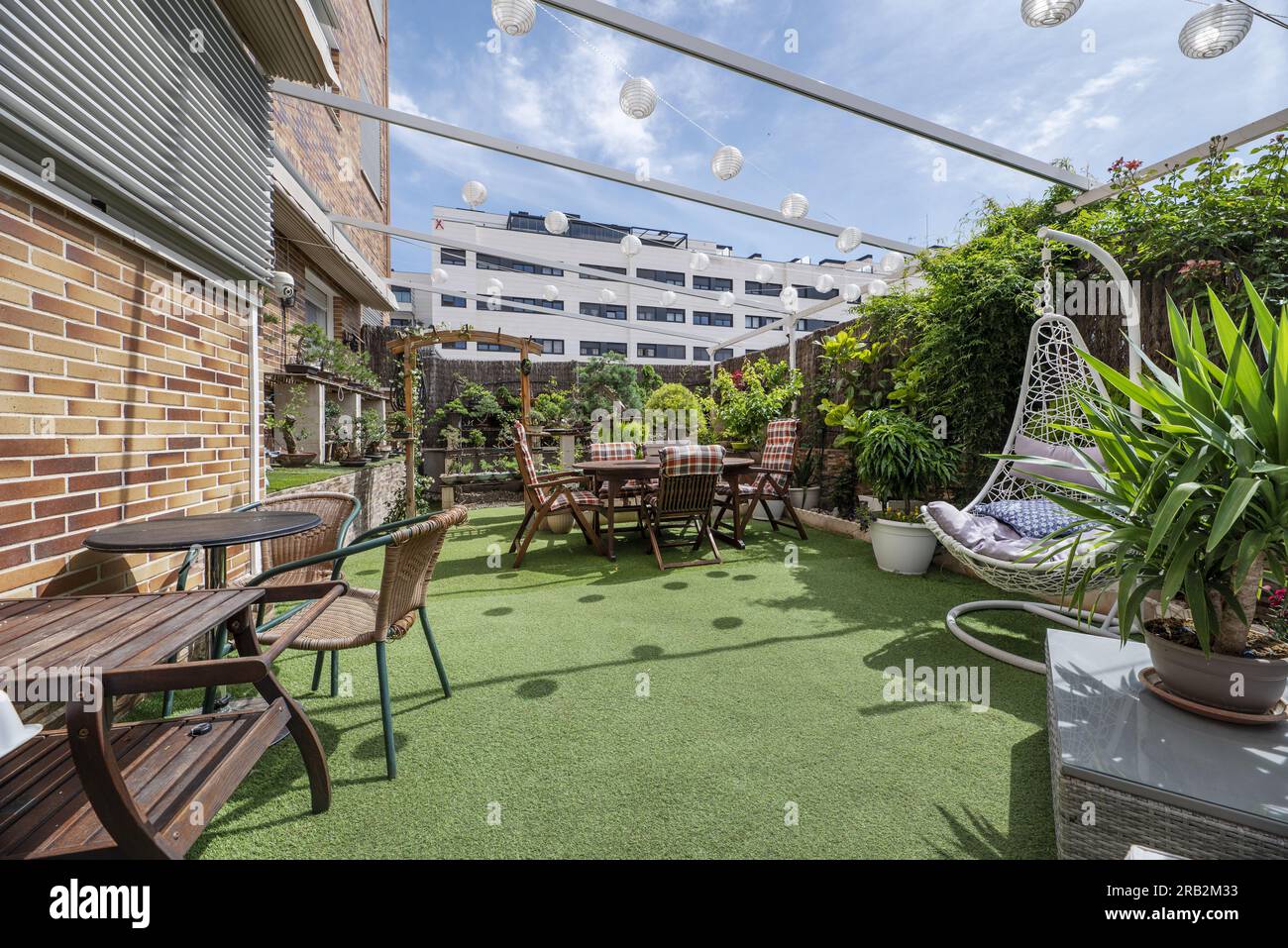 terrasse avec canapé en raphia, faux sols en herbe, table à manger en bois avec chaises assorties et beaucoup de plantes Banque D'Images