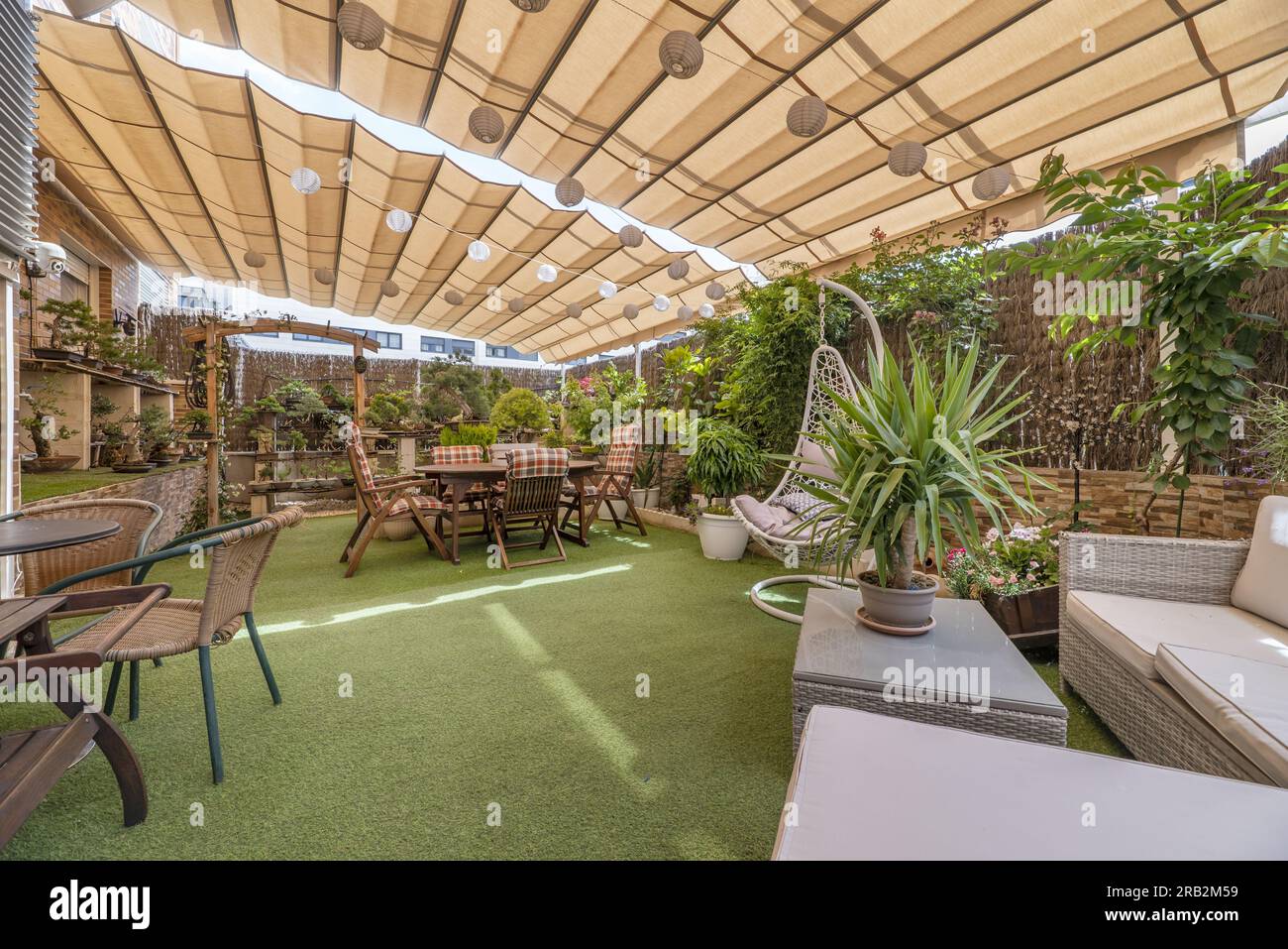 terrasse avec canapé en raphia, sols en gazon artificiel, table à manger en bois avec chaises assorties et de nombreuses plantes recouvertes d'auvent pliant Banque D'Images