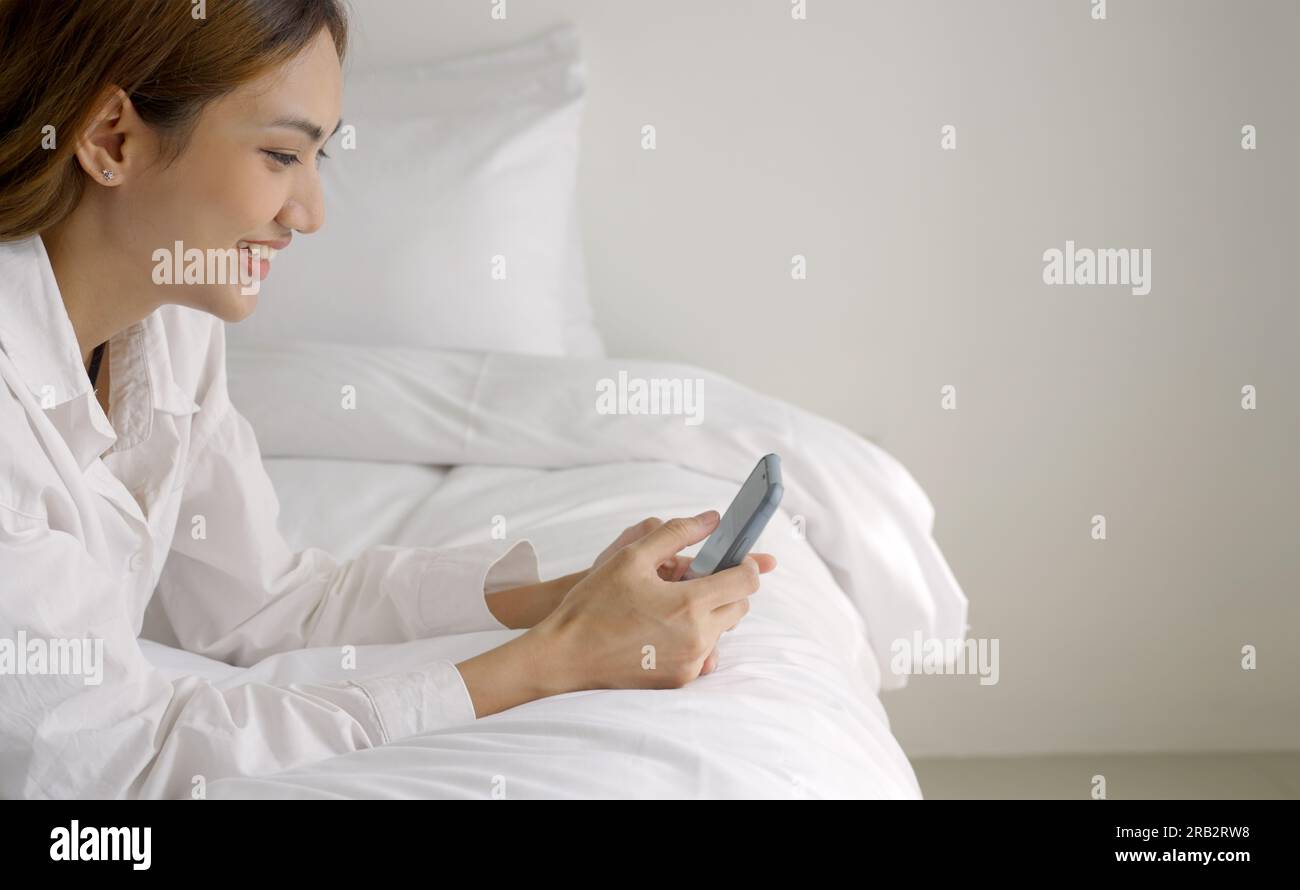 Femme détendue à l'aide d'un téléphone intelligent le matin dans le lit à la maison. Banque D'Images