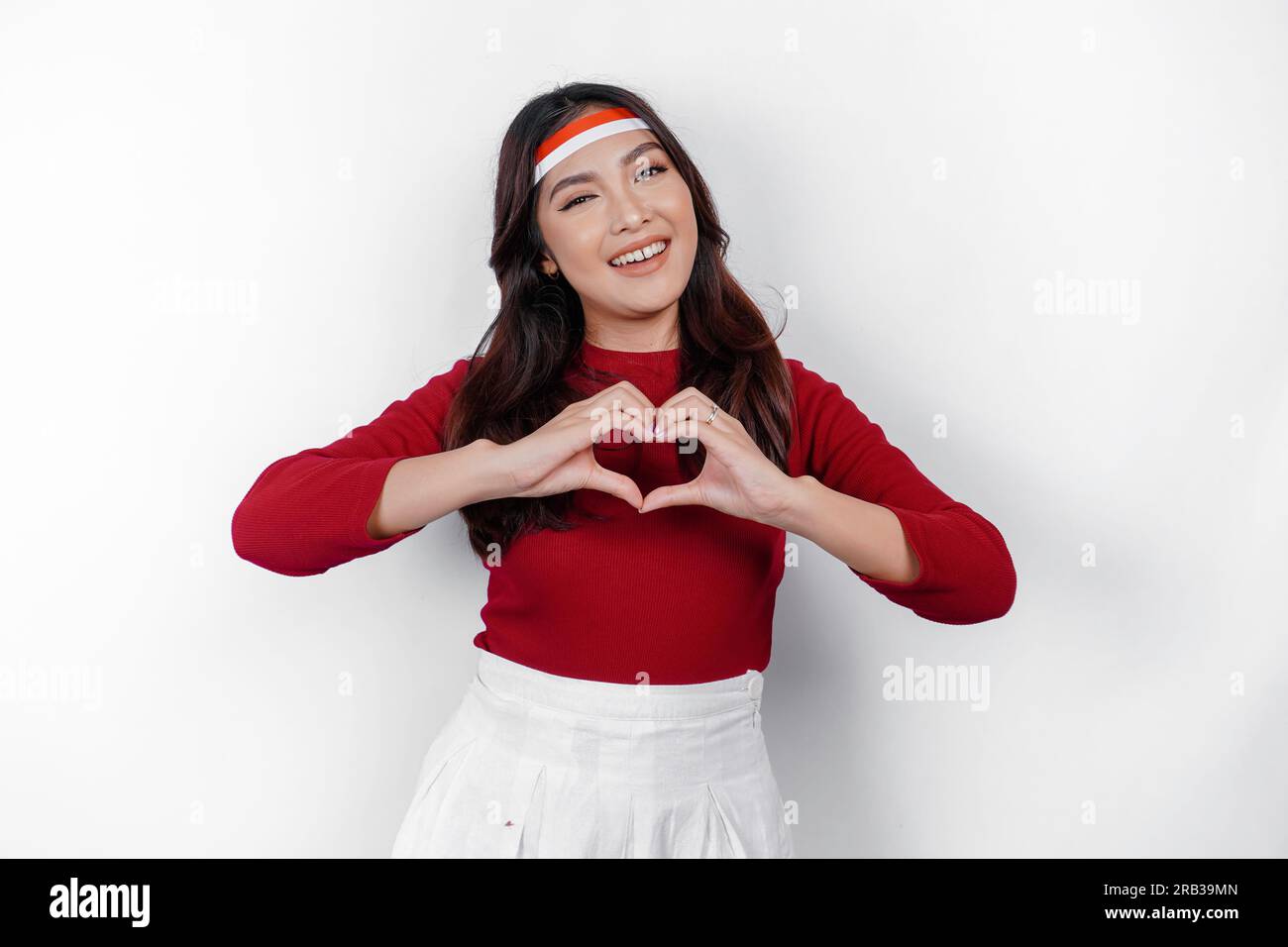 Une jeune femme asiatique portant un haut rouge ressent le nationalisme, façonne le geste du cœur exprime son amour pour l’Indonésie. Concept du jour de l'indépendance de l'Indonésie. Banque D'Images