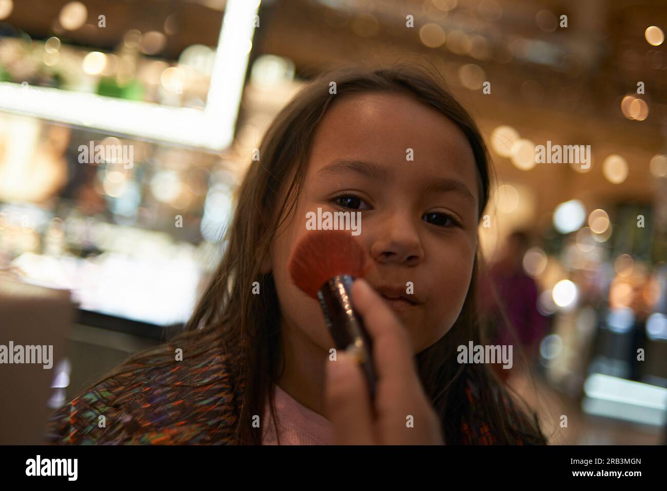 Mignonne fille asiatique essayant une brosse de maquillage pour la première fois dans un centre commercial Banque D'Images