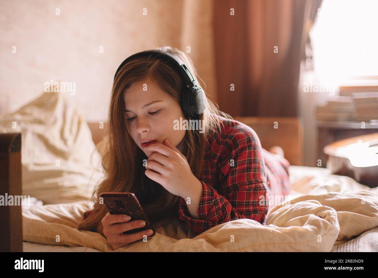 Jeune femme avec des écouteurs à l'aide d'un téléphone intelligent couché sur le lit à la maison Banque D'Images