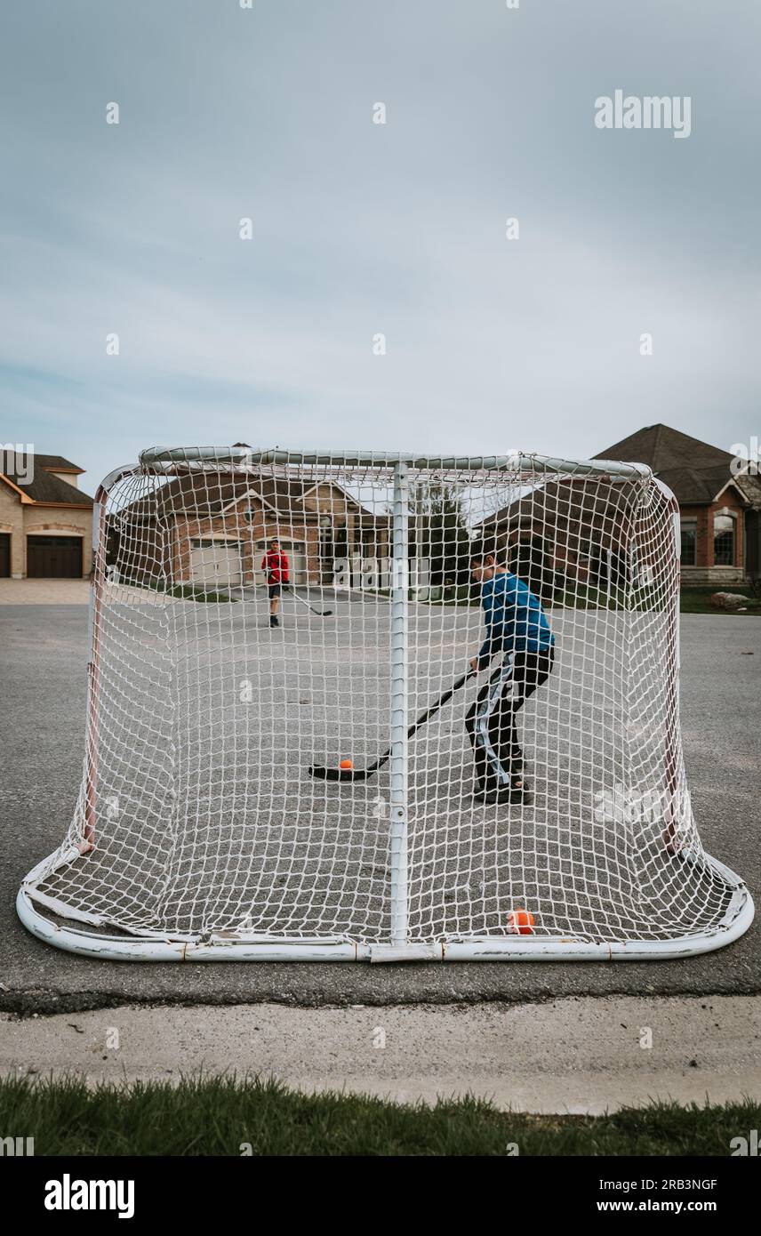 Deux garçons jouant au hockey-balle dehors dans la rue ensemble. Banque D'Images