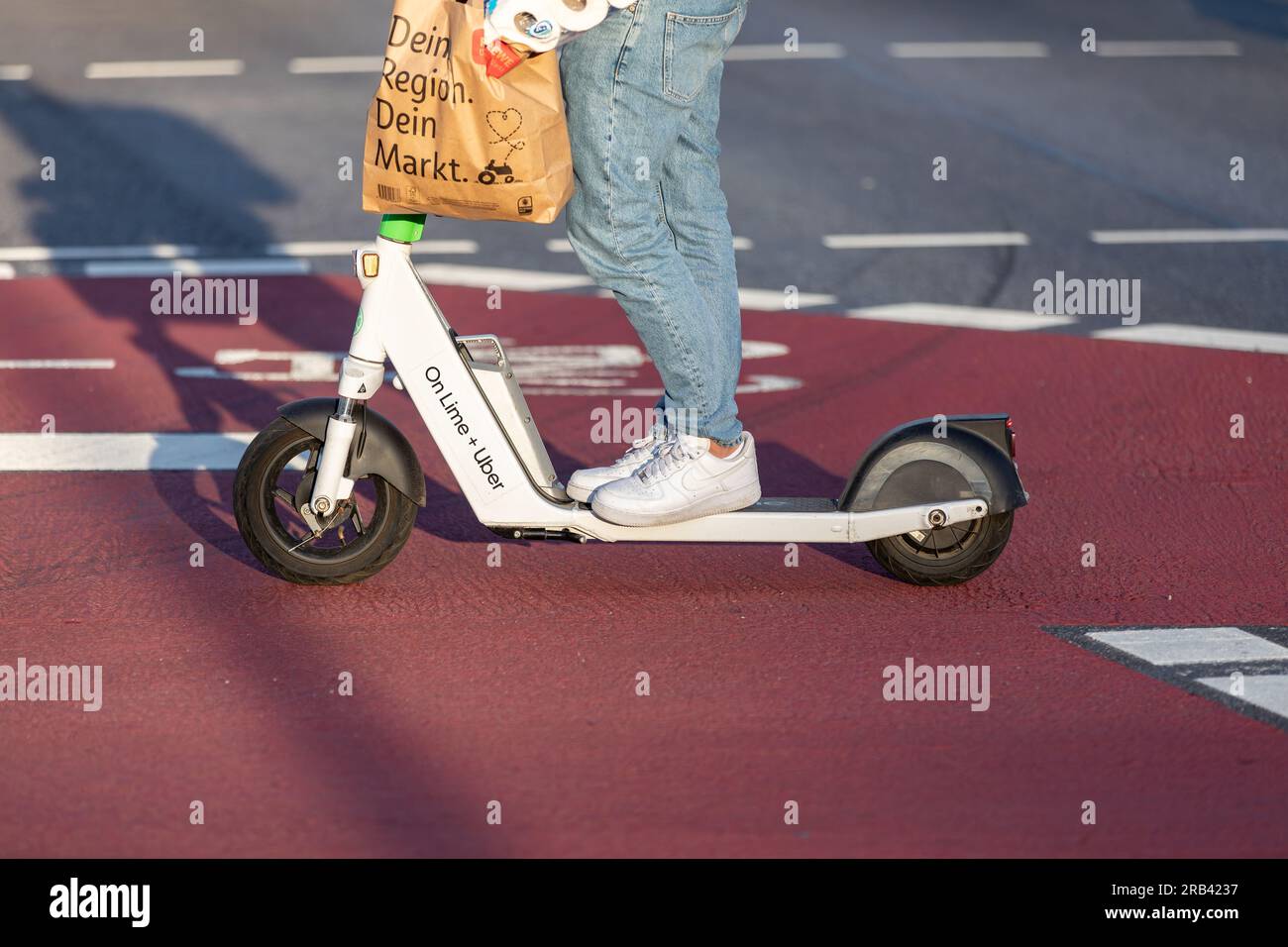 Hambourg, Allemagne - 27 avril 2023 : Homme avec sac à provisions se déplace sur scooter électrique sur piste cyclable Banque D'Images