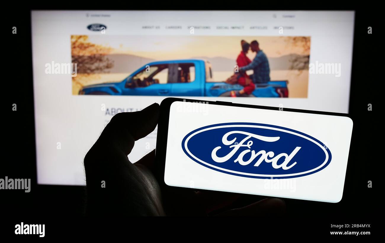 Personne tenant le smartphone avec le logo du constructeur automobile américain Ford Motor Company sur l'écran en face du site Web. Concentrez-vous sur l'affichage du téléphone. Banque D'Images